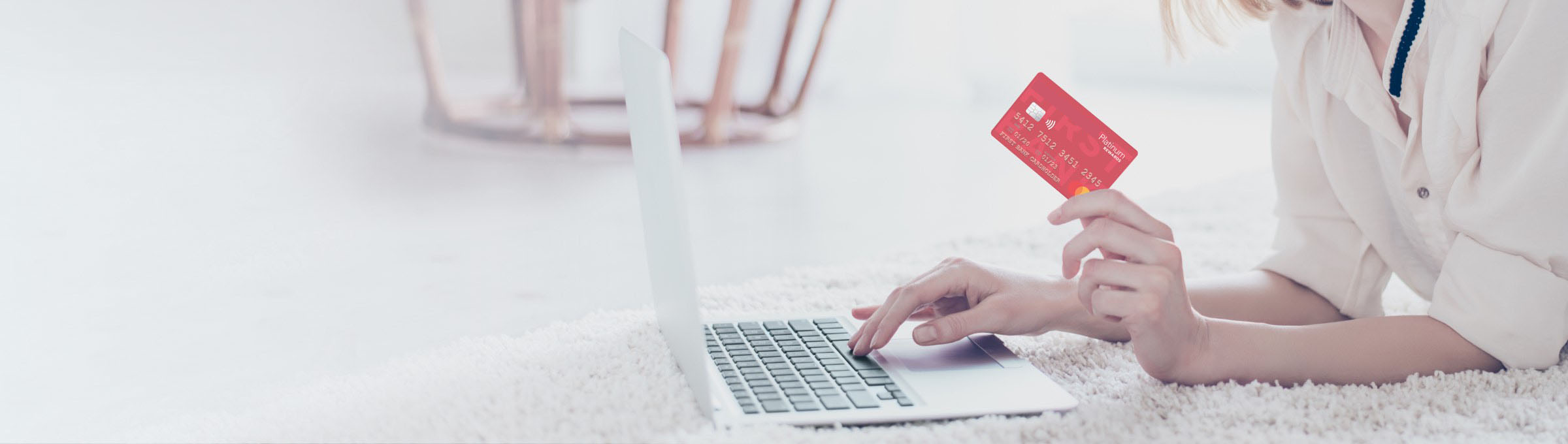 a woman holding her Sun Central Credit Union Platinum Rewards card while on the computer.